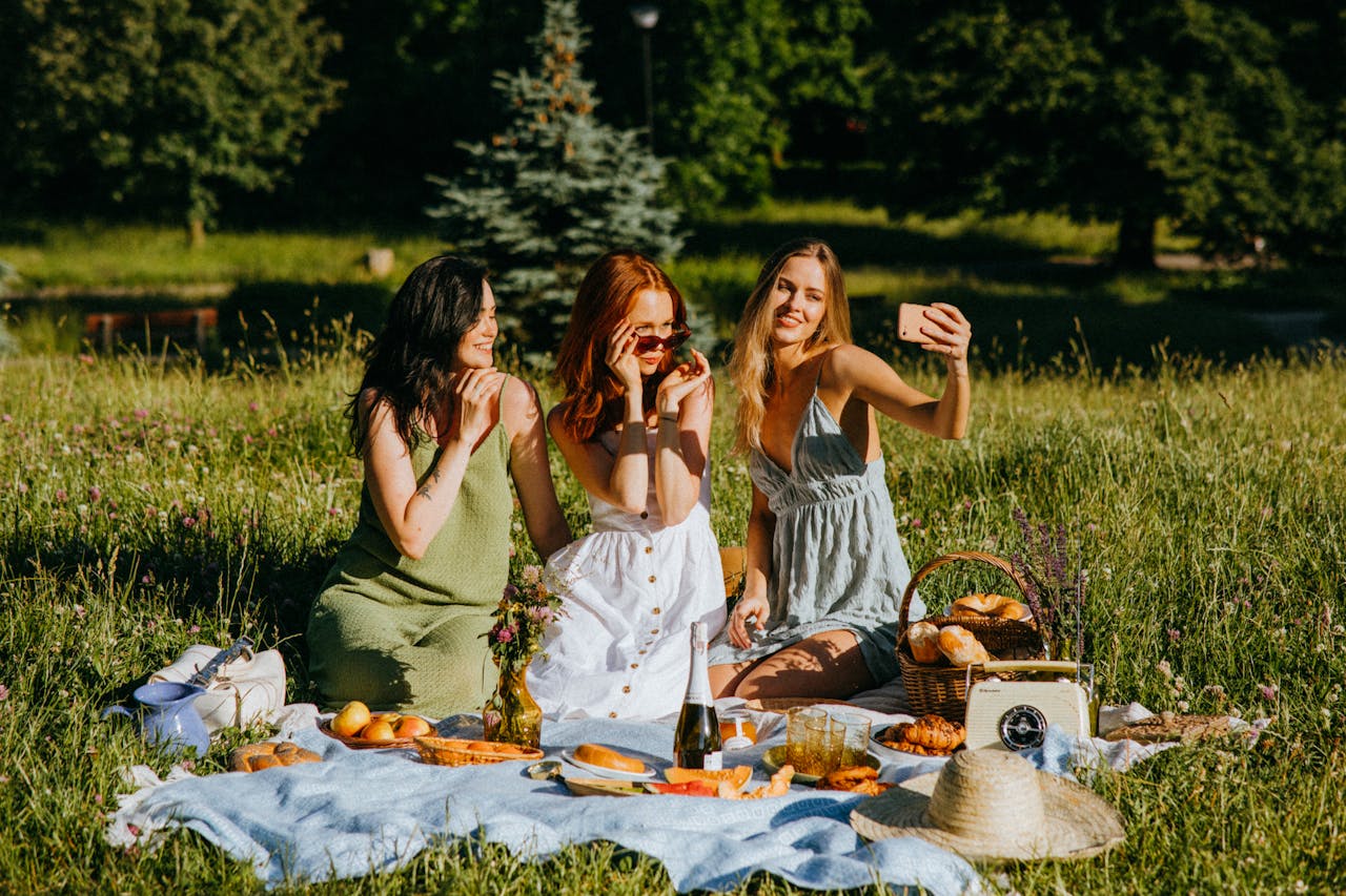 Mastering the First Impression: Your intriguing post title goes here Three women enjoying a summer picnic in a park, capturing a selfie together.